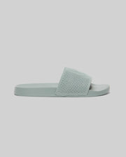The KIDS KNIT SLIDES - B0A377F200 by Psycho Bunny feature a light blue knit textile, thick textured strap, flat sole, and an ergonomically molded footbed. Shown on a plain light gray background.
