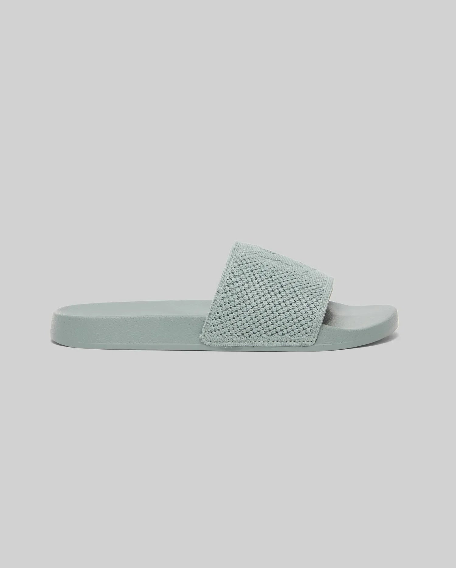 The KIDS KNIT SLIDES - B0A377F200 by Psycho Bunny feature a light blue knit textile, thick textured strap, flat sole, and an ergonomically molded footbed. Shown on a plain light gray background.