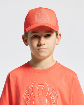 A young person sports a Psycho Bunny KIDS MELBOURNE GRAPHIC TRUCKER HAT - B0A548F200 and a matching t-shirt featuring an embroidered rabbit icon. The background is plain white.