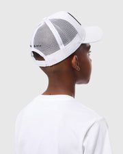A person in a white t-shirt and a Psycho Bunny KIDS BUNNY PATCH TRUCKER CAP - B0A965C200 is seen from the back against a light grey background. The cap has the recognizable Bunny logo patch, with short hair visible beneath it.