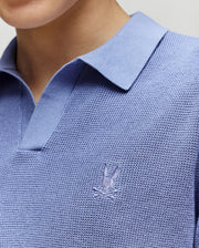 A close-up of a person wearing the Psycho Bunny KIDS LEETON JOHNNY COLLAR KNIT POLO (B0E562F200) in light blue, featuring a stitched bunny and crossed sticks logo on the chest. The person's face is not visible.