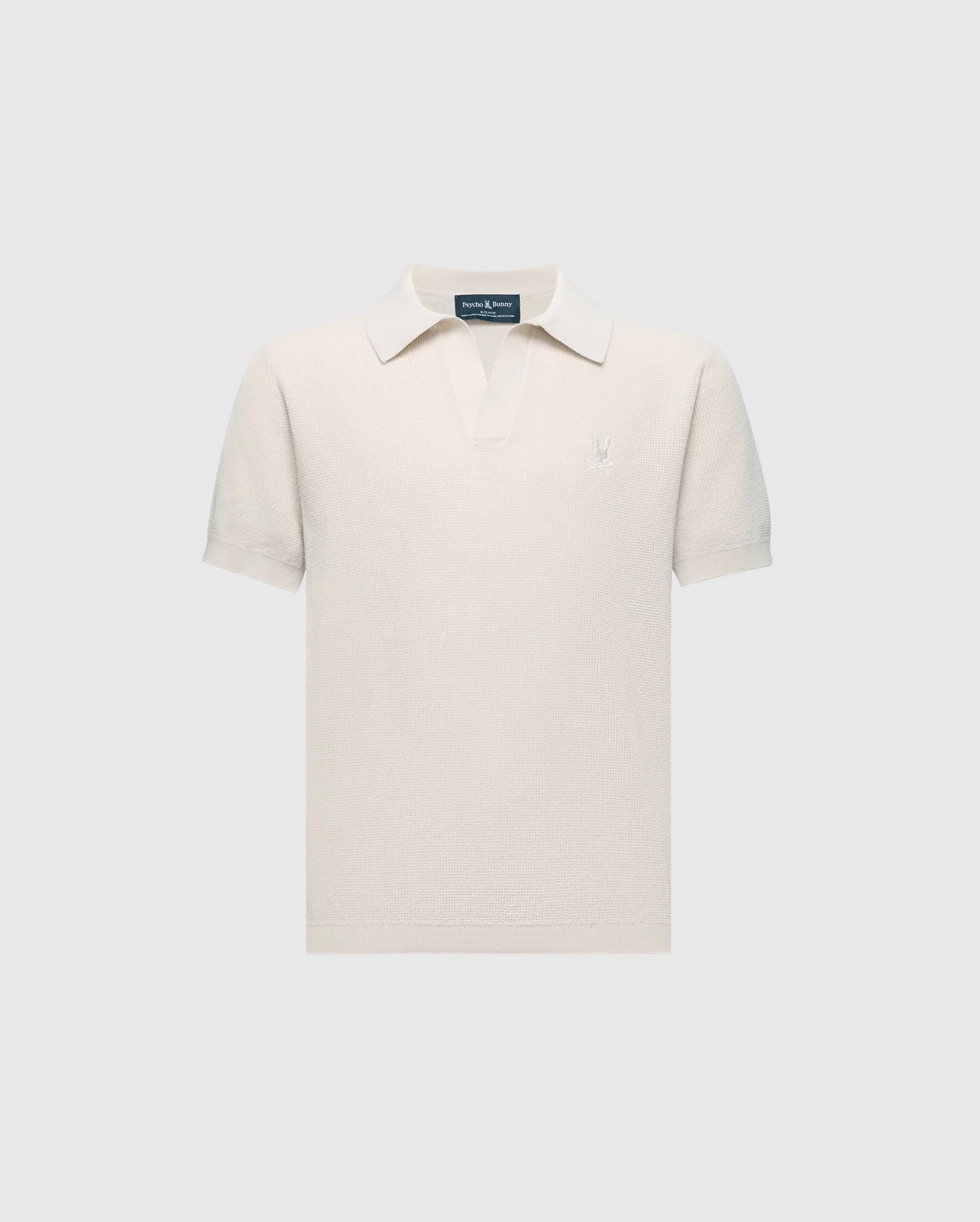 The KIDS LEETON JOHNNY COLLAR KNIT POLO - B0E562F200 by Psycho Bunny is a cream-colored terry cloth shirt featuring short sleeves, a small collar, and an embroidered bunny logo on the left chest. Made from breathable cotton with a textured look, it’s set against a plain backdrop.