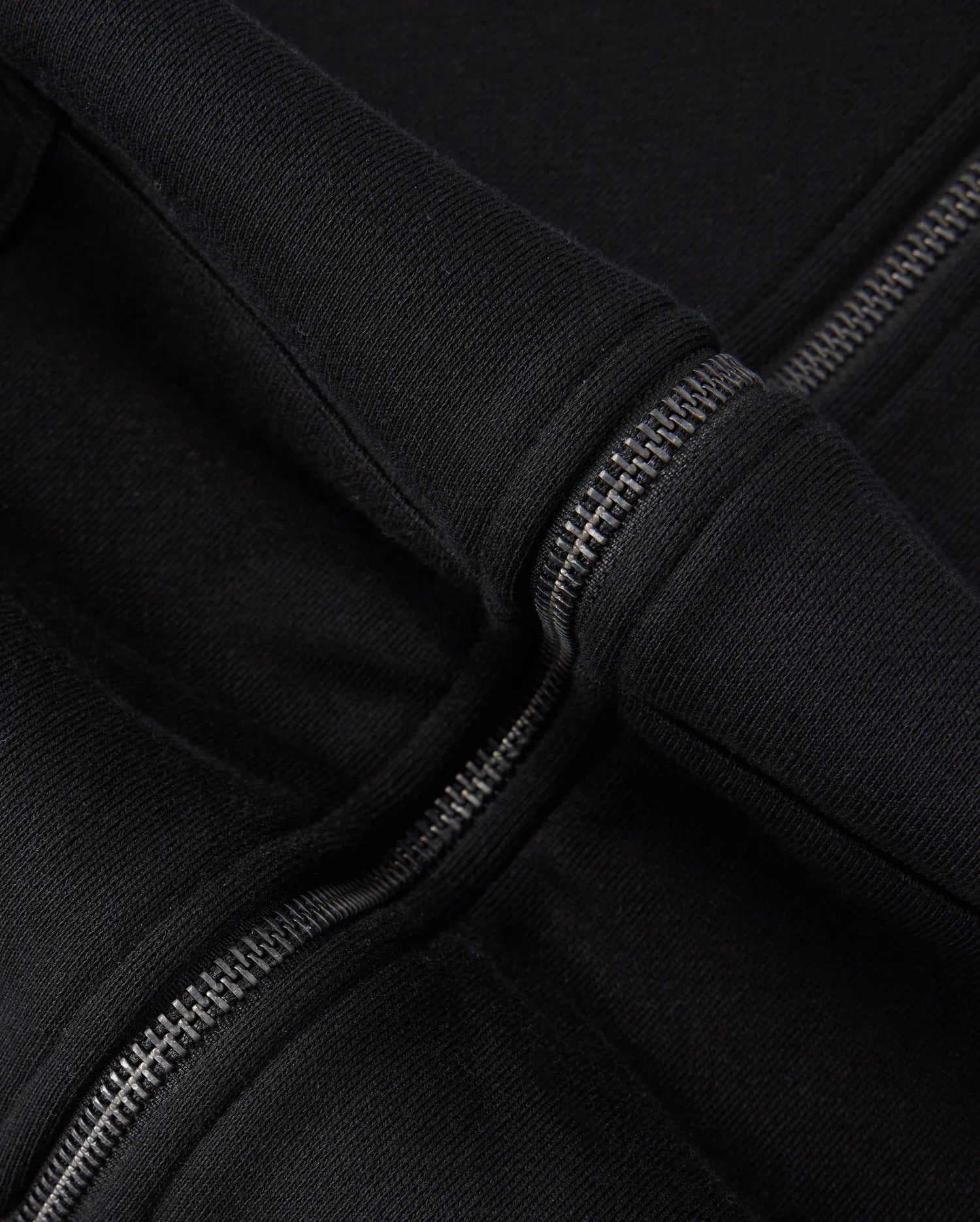 Close-up image of the Psycho Bunny KIDS LEVY ZIP FLEECE HOODIE - B0H720D200 in black, highlighting the metal zipper and the seam where the hood attaches to the main body of the garment. The thick, fleece-lined fabric appears soft and warm, ideal for little ones.