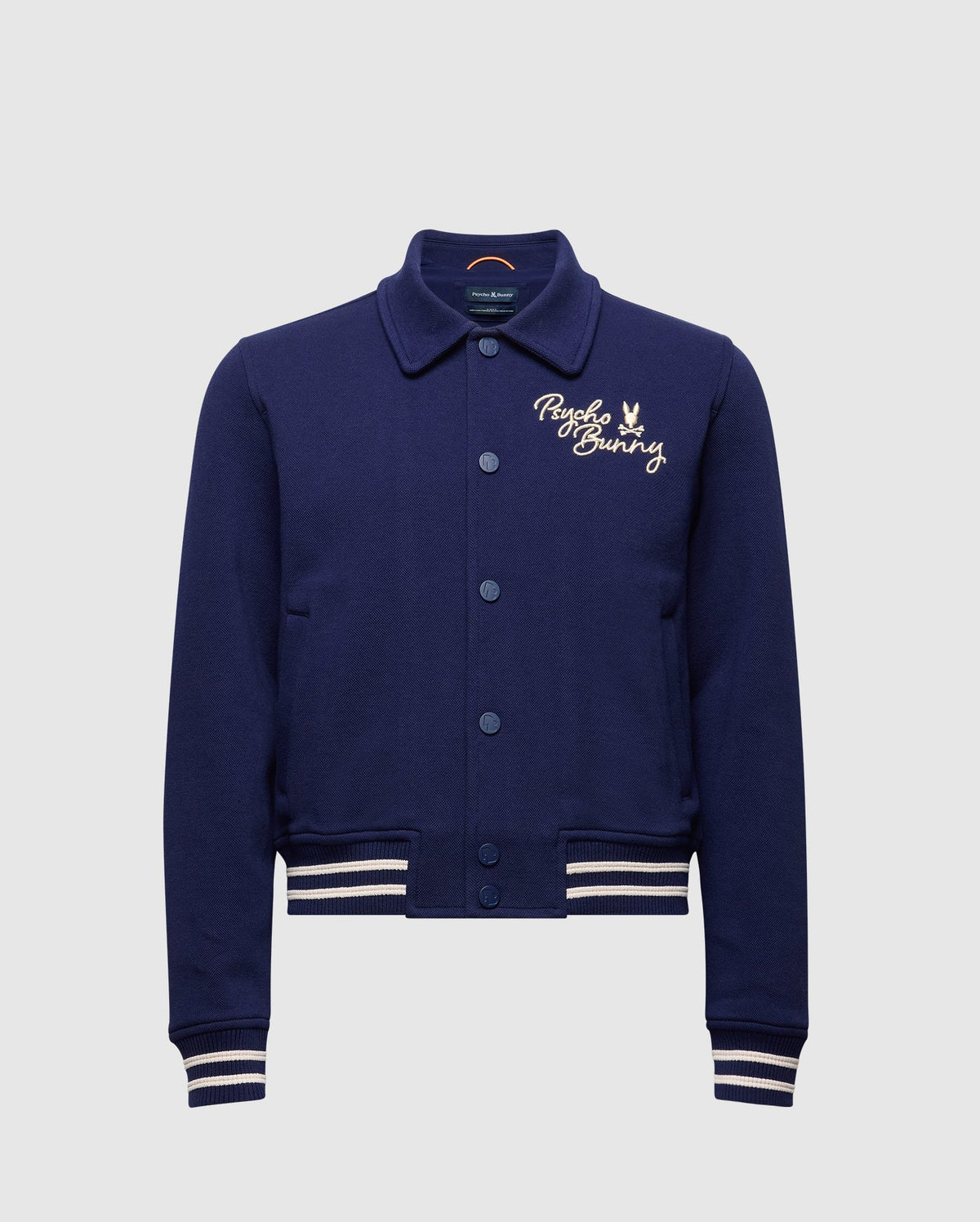The Psycho Bunny KIDS DESERT COACH BOMBER JACKET (B0J428F200) in Evening Blue features white striped cuffs and hem, button-up front, and a small embroidered bunny logo on the left chest.