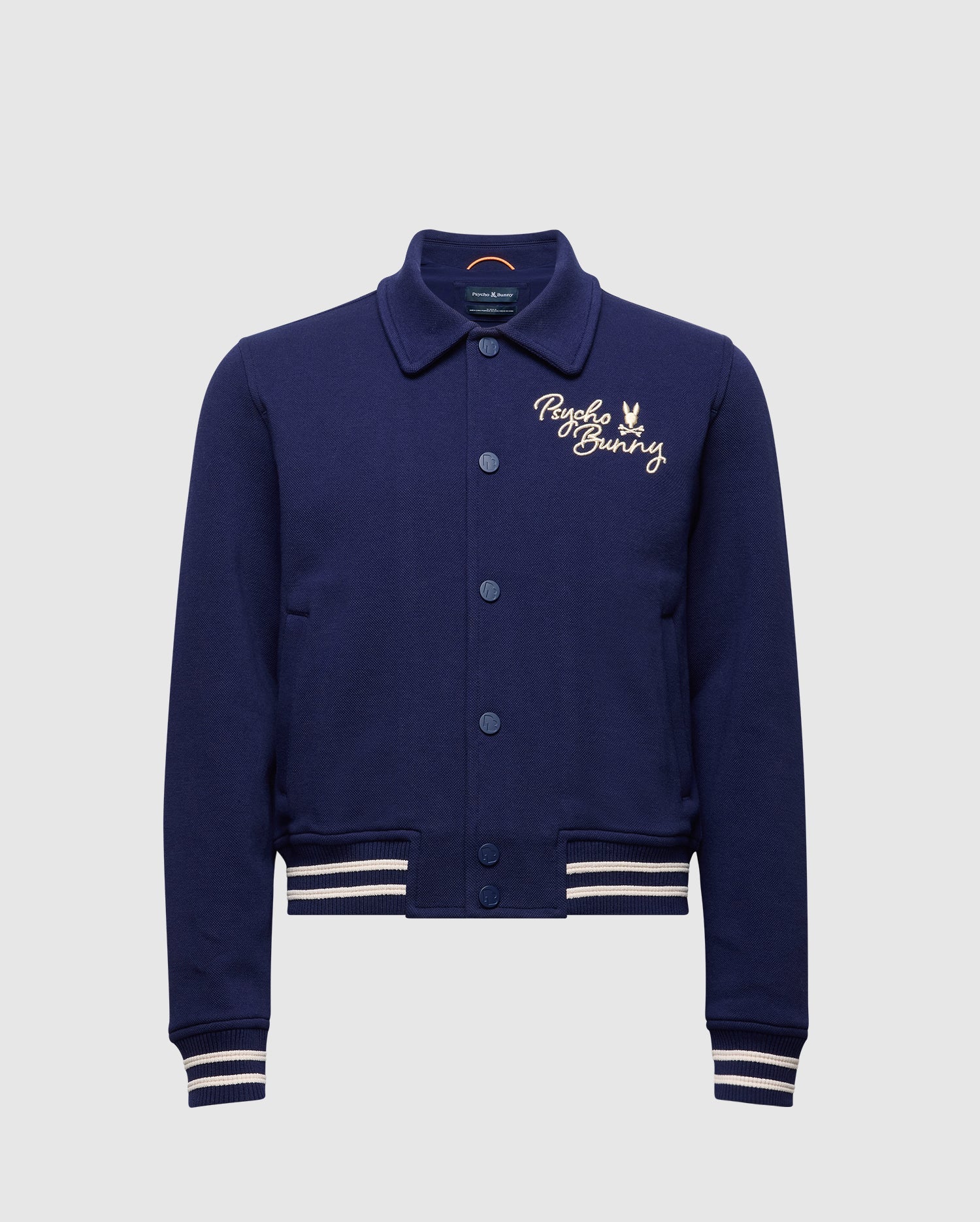 The Psycho Bunny KIDS DESERT COACH BOMBER JACKET (B0J428F200) in Evening Blue features white striped cuffs and hem, button-up front, and a small embroidered bunny logo on the left chest.