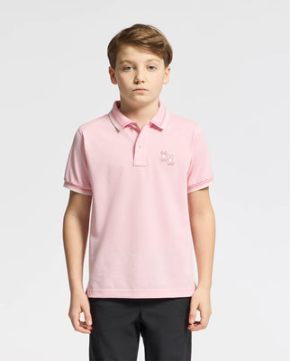A young person models the Psycho Bunny KIDS ELLIOT PIQUE POLO in light pink, crafted from soft Pima cotton with a small embroidered logo on the chest. They pair it with black pants against a plain white background, exuding simplicity and comfort.