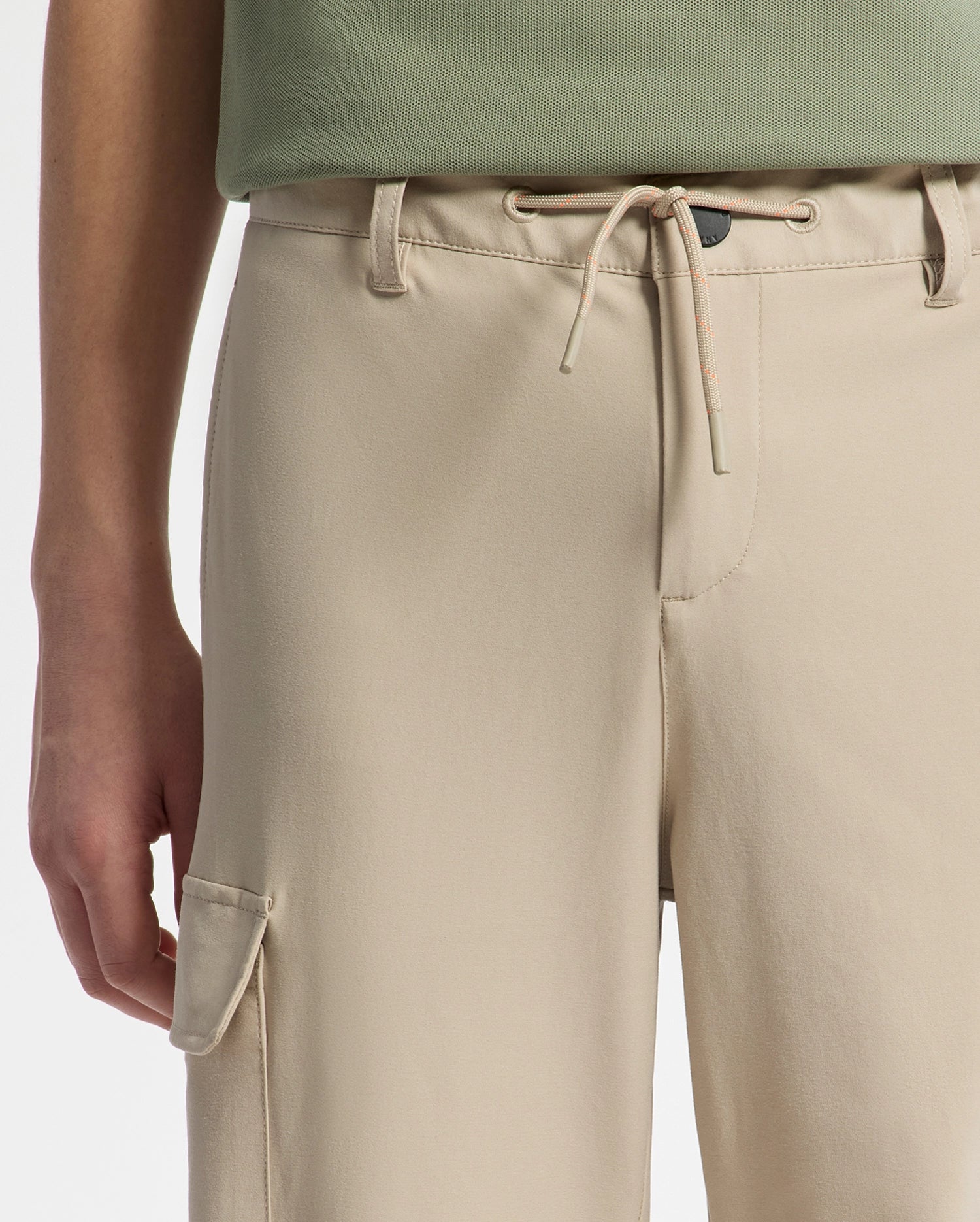 The image shows a person wearing Psycho Bunny's KIDS GREEN VALLEY CARGO PANT (B0P199E200) with a drawstring waist and spacious side pocket. The pants are shown from the lower torso on a plain white background, paired with a light green shirt.