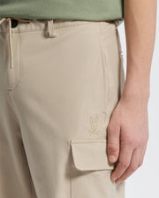 A person wearing Psycho Bunny's KIDS GREEN VALLEY CARGO PANT - B0P199E200, complete with a practical pocket featuring a small rabbit logo. The hand rests nearby, highlighting its design against a plain white background.