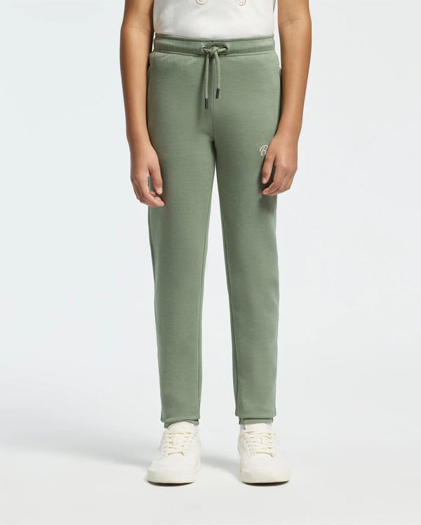 A child wearing Psycho Bunny's KIDS DESERT EMBROIDERED MODAL SWEATPANT (B0P489F200) in light green, featuring an embroidered wordmark and a drawstring, is paired with a light t-shirt and white sneakers. The background is plain and neutral.