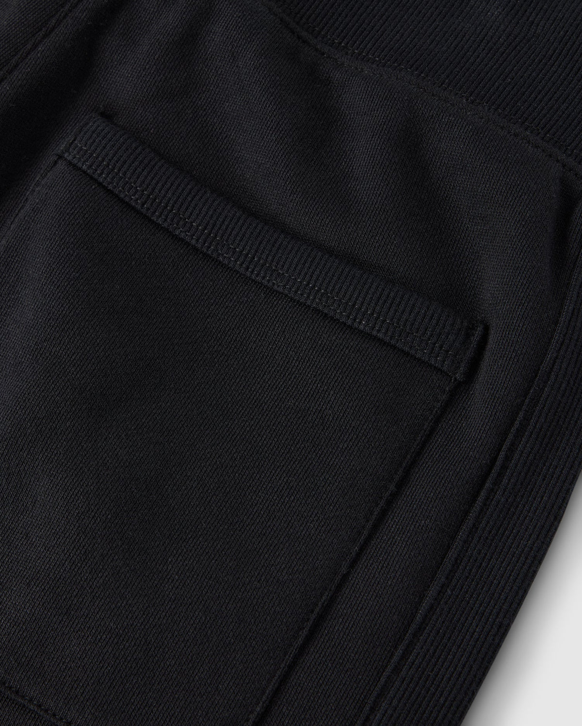 Close-up of a textured black fabric pocket with visible stitching on cozy fleece, highlighting detailed craftsmanship on Psycho Bunny's KIDS LEVY ESSENTIAL FLEECE SWEATPANT - B0P721D200.