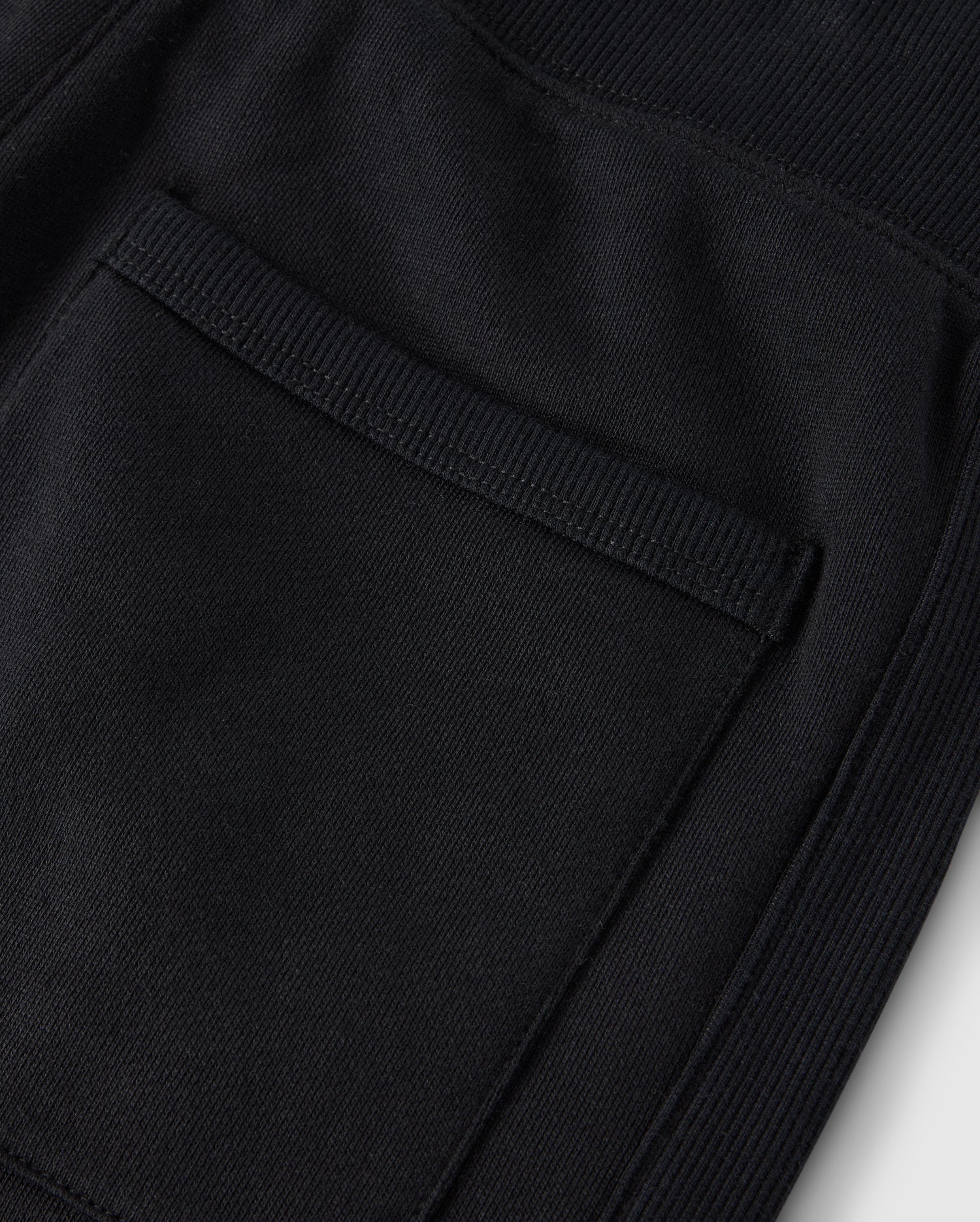Close-up of a textured black fabric pocket with visible stitching on cozy fleece, highlighting detailed craftsmanship on Psycho Bunny's KIDS LEVY ESSENTIAL FLEECE SWEATPANT - B0P721D200.