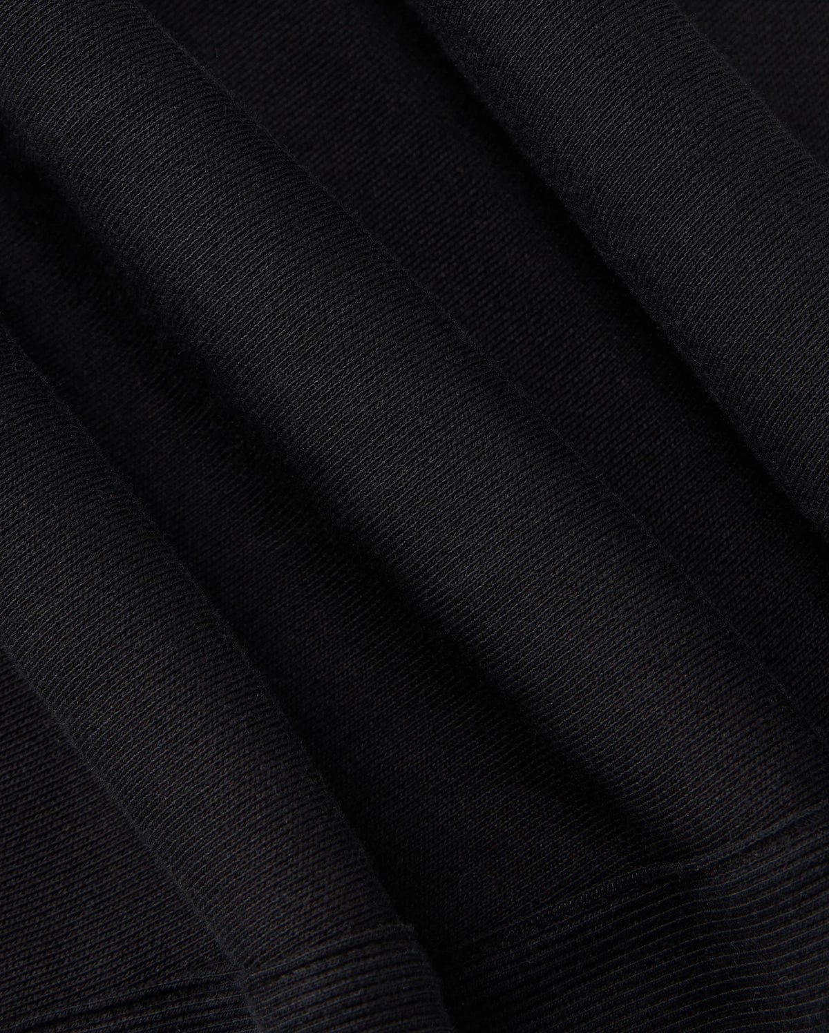 A close-up of the Psycho Bunny KIDS LEVY ESSENTIAL FLEECE SWEATPANT (B0P721D200) in black showcases a textured knit pattern with soft folds and dense weave, suggesting the warmth and comfort ideal for cozy fleece fabric.
