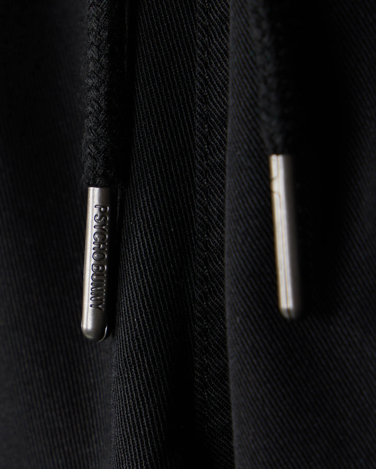 Close-up of black KIDS WILLIS STRETCH TENCEL SHORT featuring two drawstrings with silver metal tips engraved with "Bunny Psycho." The texture and slim fit highlight the intertwined threads, complemented by a subtle embroidered Bunny logo for playful sophistication.