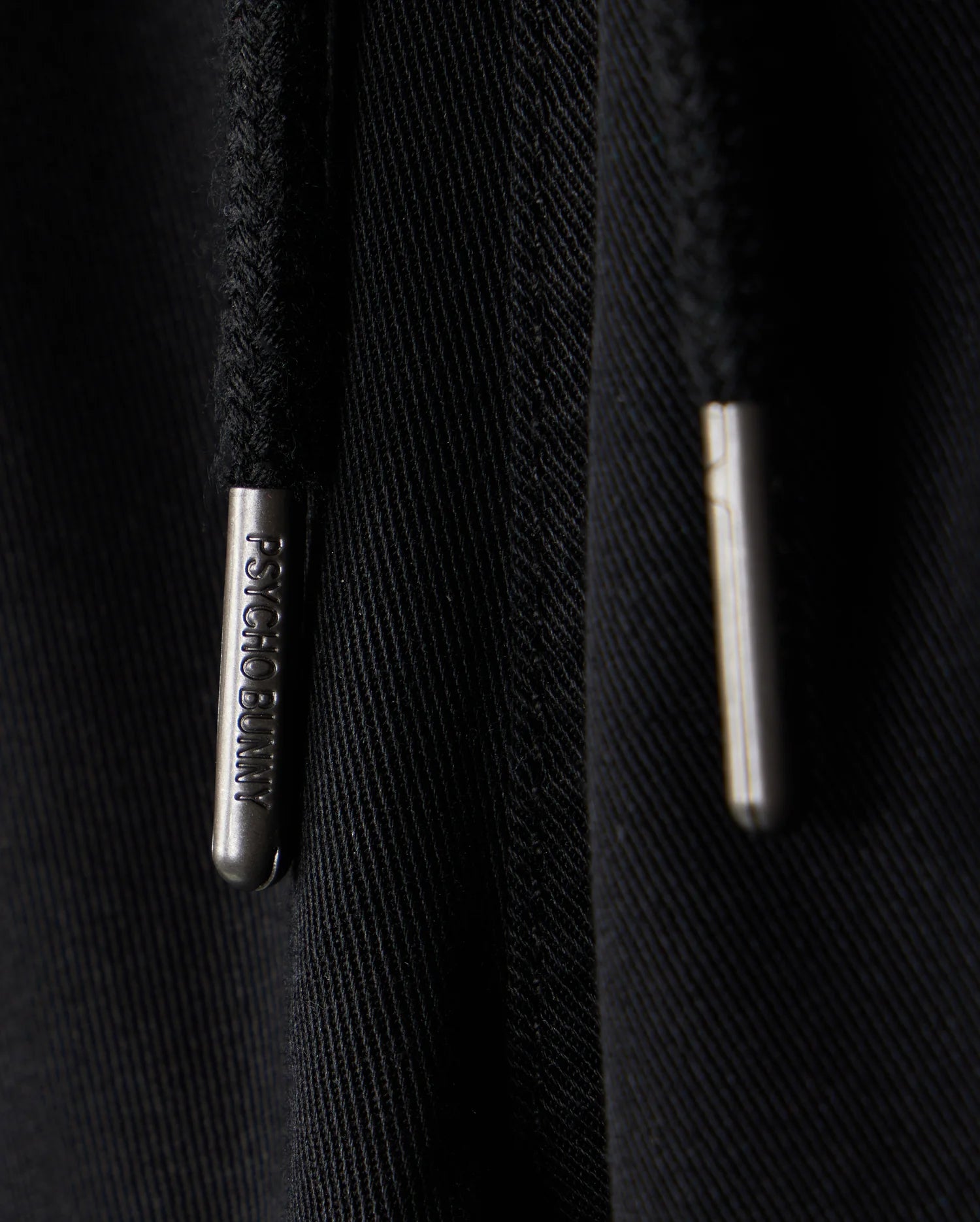 Close-up of black KIDS WILLIS STRETCH TENCEL SHORT featuring two drawstrings with silver metal tips engraved with "Bunny Psycho." The texture and slim fit highlight the intertwined threads, complemented by a subtle embroidered Bunny logo for playful sophistication.