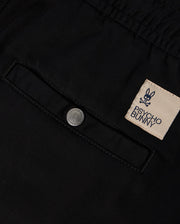 Close-up of a black fabric with a buttoned pocket, featuring an embroidered Psycho Bunny label with the bunny skull logo. The KIDS WILLIS STRETCH TENCEL SHORT (B0R239Y1WB) offers a slim fit design that incorporates Stretch TENCEL™ for comfort and style.