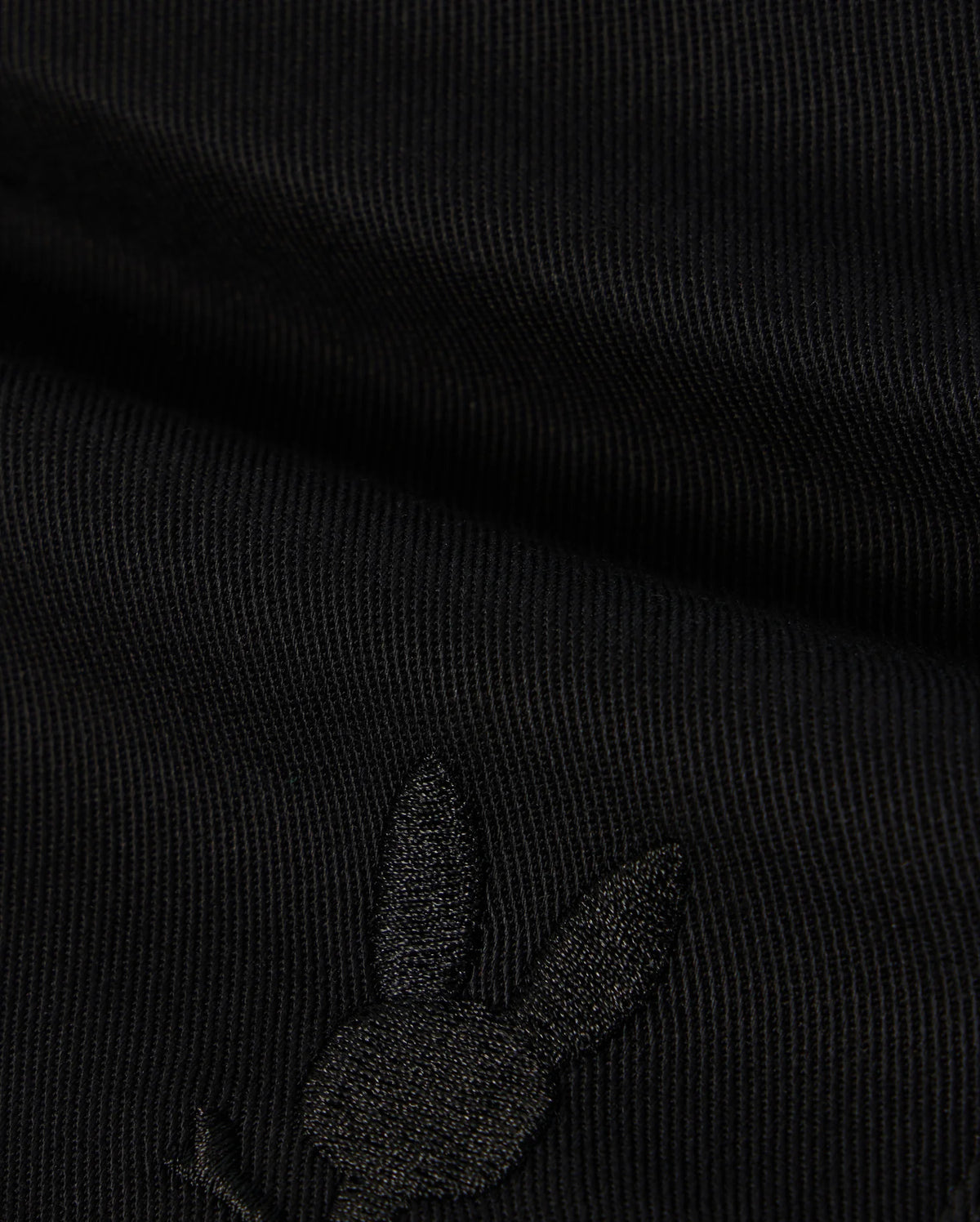 A close-up of the black KIDS WILLIS STRETCH TENCEL SHORT by Psycho Bunny shows ribbed fabric with an embroidered rabbit head silhouette. Visible texture and stitching highlight its supple finish and refined style. (B0R239Y1WB).
