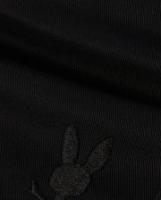 A close-up of the black KIDS WILLIS STRETCH TENCEL SHORT by Psycho Bunny shows ribbed fabric with an embroidered rabbit head silhouette. Visible texture and stitching highlight its supple finish and refined style. (B0R239Y1WB).