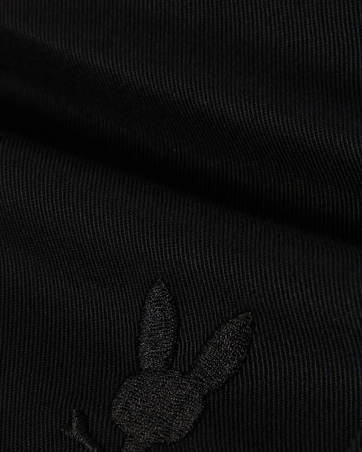 A close-up of the black KIDS WILLIS STRETCH TENCEL SHORT by Psycho Bunny shows ribbed fabric with an embroidered rabbit head silhouette. Visible texture and stitching highlight its supple finish and refined style. (B0R239Y1WB).