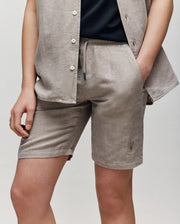 A child models the Psycho Bunny KIDS set: a matching light beige short-sleeve shirt and linen-cotton breezy shorts with a drawstring waist, one hand in their pocket, against a plain background.