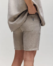 A person wears Psycho Bunny KIDS beige breezy shorts with a matching shirt, standing against a plain light background with one hand in their back pocket.