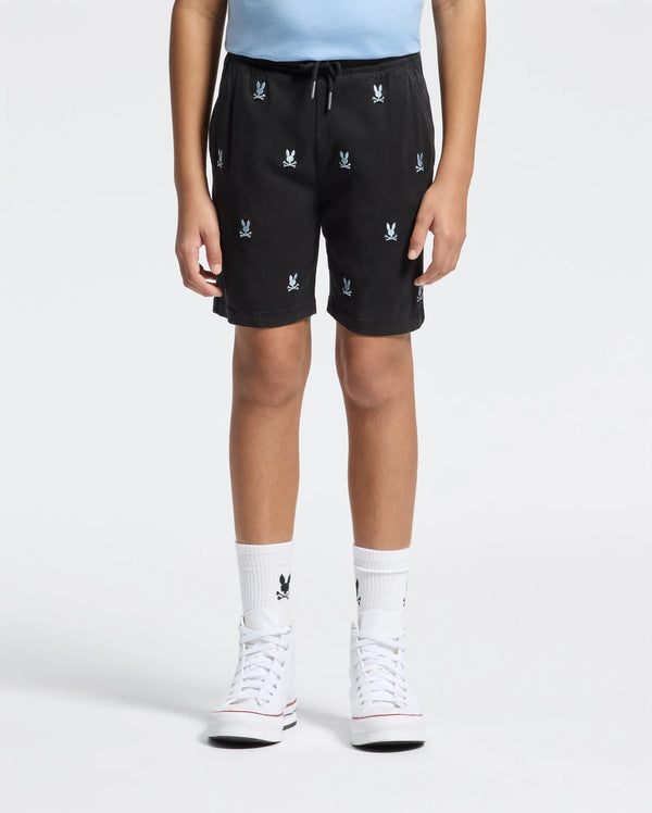 A child wears Psycho Bunny KIDS ALL OVER WILLIS STRETCH TENCEL SHORTS (B0R559F200) featuring white bunny logos, a light blue shirt, matching bunny socks, and white high-top sneakers, standing against a plain white background.