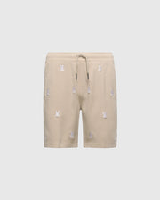 The KIDS ALL OVER WILLIS STRETCH TENCEL SHORT by Psycho Bunny, B0R559F200, features beige fabric with an elastic waistband, drawstring, and small white embroidered motifs. Its stretch Tencel blend offers comfort and sophistication against a plain white background.