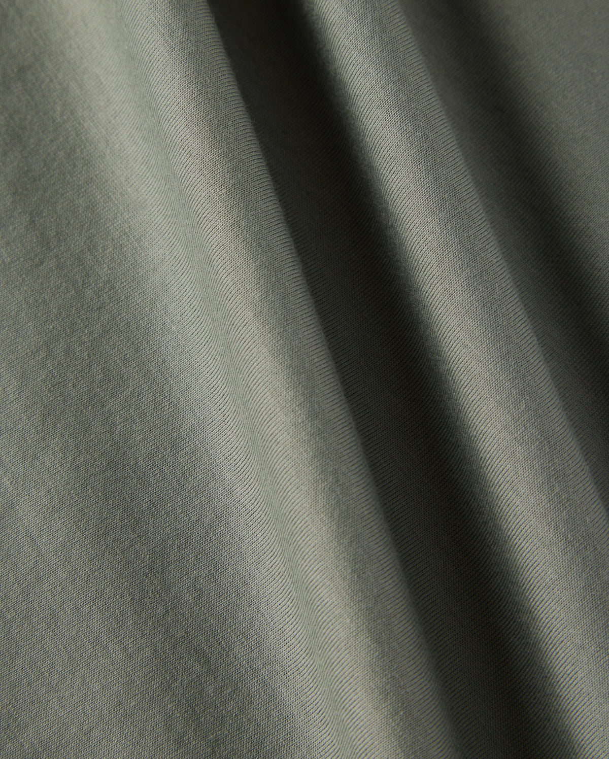 Close-up of a textured olive-green fabric with soft folds, showcasing the material's subtle creases and smooth surface, reminiscent of the Psycho Bunny KIDS CLASSIC CREW NECK TEE - B0U014B200, perfect for back-to-school outfits.