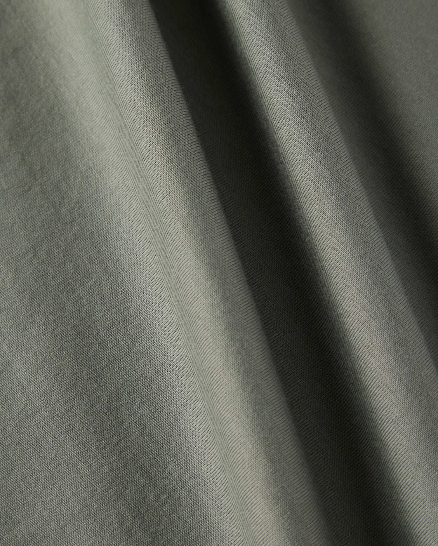 Close-up of a textured olive-green fabric with soft folds, showcasing the material's subtle creases and smooth surface, reminiscent of the Psycho Bunny KIDS CLASSIC CREW NECK TEE - B0U014B200, perfect for back-to-school outfits.