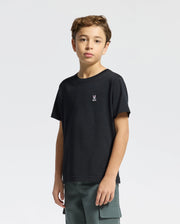 A young boy with wavy hair wears Psycho Bunny's KIDS CLASSIC CREW NECK TEE (B0U014CRPC) in black, featuring a small embroidered rabbit logo. Made from 100% Pima cotton, it pairs perfectly with his green cargo pants against the plain white background.