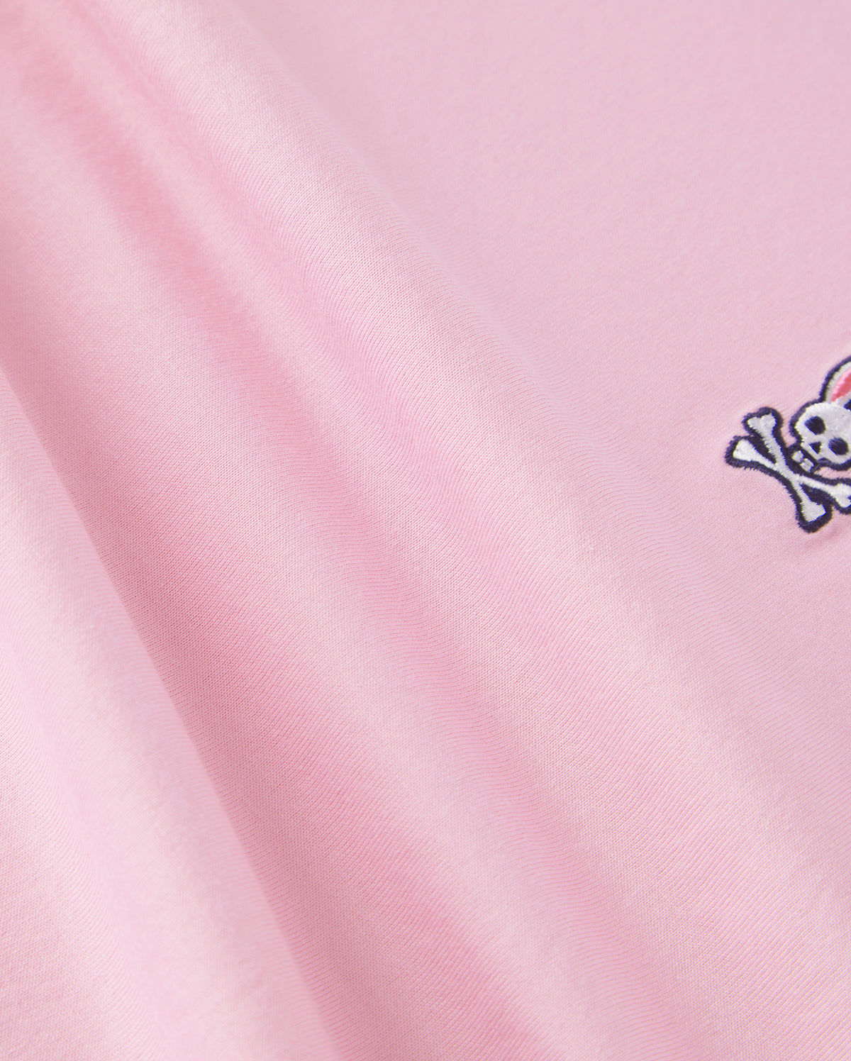 The Psycho Bunny KIDS CLASSIC CREW NECK TEE - B0U014CRPC is made of 100% Pima cotton, showcasing a pink fabric with an embroidered skull and crossbones. It offers a smooth texture and soft look, ideal for back-to-school outfits.