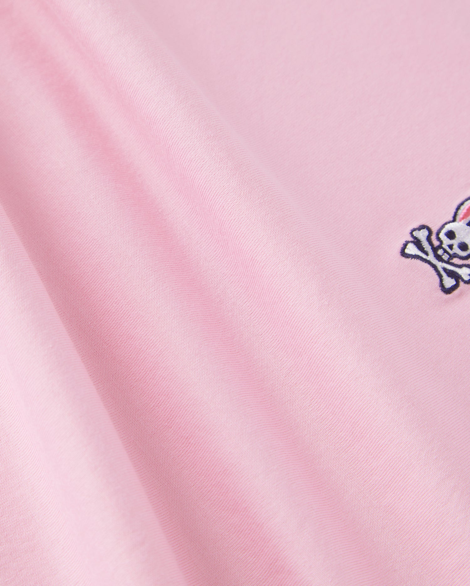The Psycho Bunny KIDS CLASSIC CREW NECK TEE - B0U014CRPC is made of 100% Pima cotton, showcasing a pink fabric with an embroidered skull and crossbones. It offers a smooth texture and soft look, ideal for back-to-school outfits.
