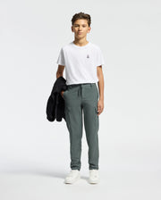 A young person stands against a plain background, wearing the Psycho Bunny KIDS CLASSIC CREW NECK TEE, green cargo pants, and white sneakers. They hold a black jacket on their shoulder, subtly nodding to the Classic Psycho Bunny logo.