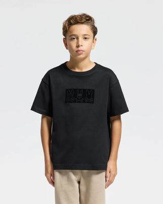 A young boy with curly hair is wearing the Psycho Bunny KIDS ROMIO HEAVY WEIGHT RELAXED FIT TEE - B0U110E200, which features three bunny outlines on the front. He stands against a plain white background, and the heavy Pima cotton tee pairs perfectly with his beige pants.
