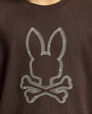 A close-up of the Psycho Bunny KIDS MONARC FRONT BUNNY GRAPHIC TEE - B0U211E200, made from soft Pima cotton, features a white geometric design of a rabbit's head with ears placed over two crossed bones on its rich dark brown fabric.