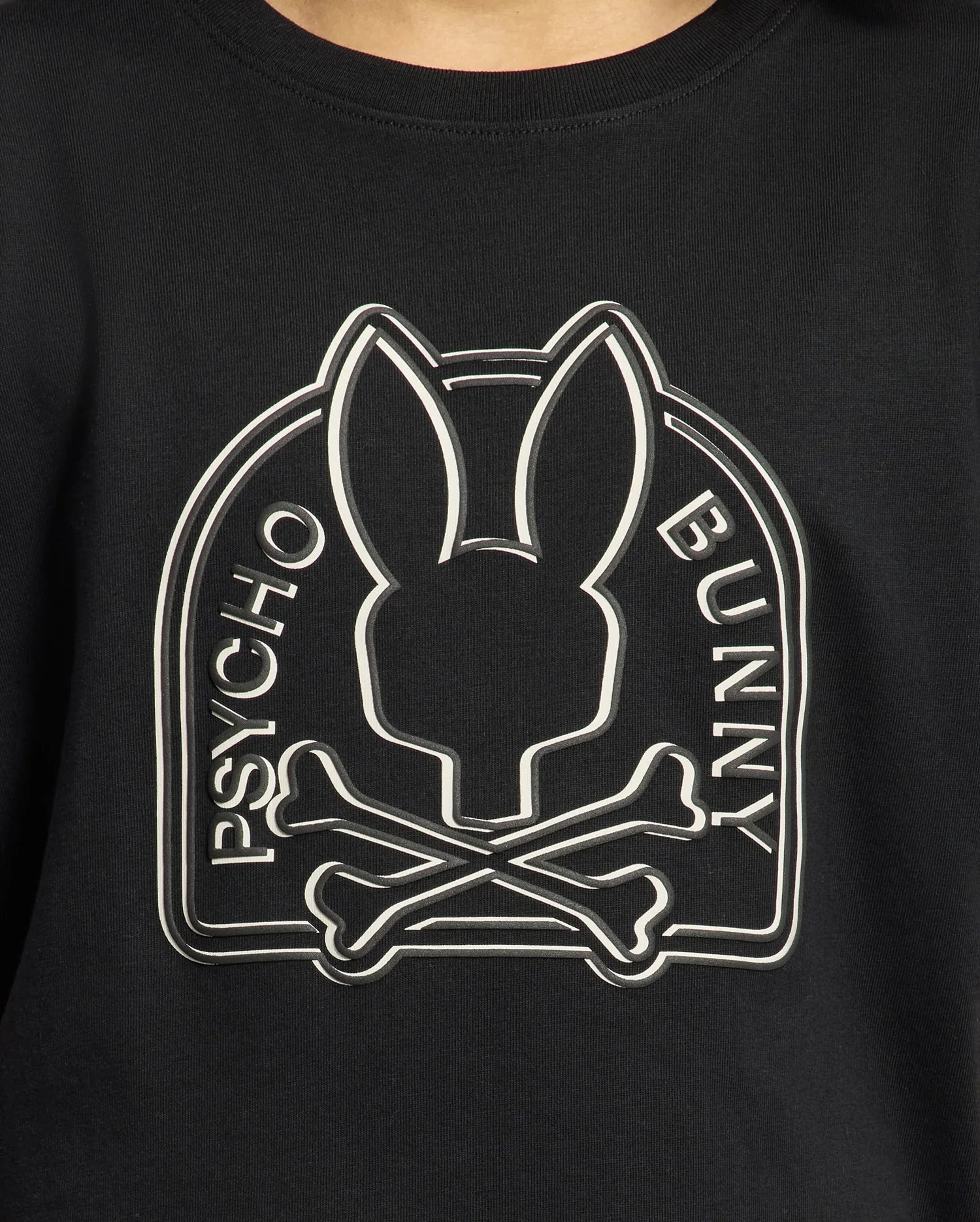 Close-up of the black KIDS MELBOURNE GRAPHIC TEE - B0U410F200 by Psycho Bunny, showcasing a logo with a stylized bunny head above crossed bones. Made from luxurious Peruvian Pima cotton, "Psycho Bunny" is elegantly written along the sides of the logo.