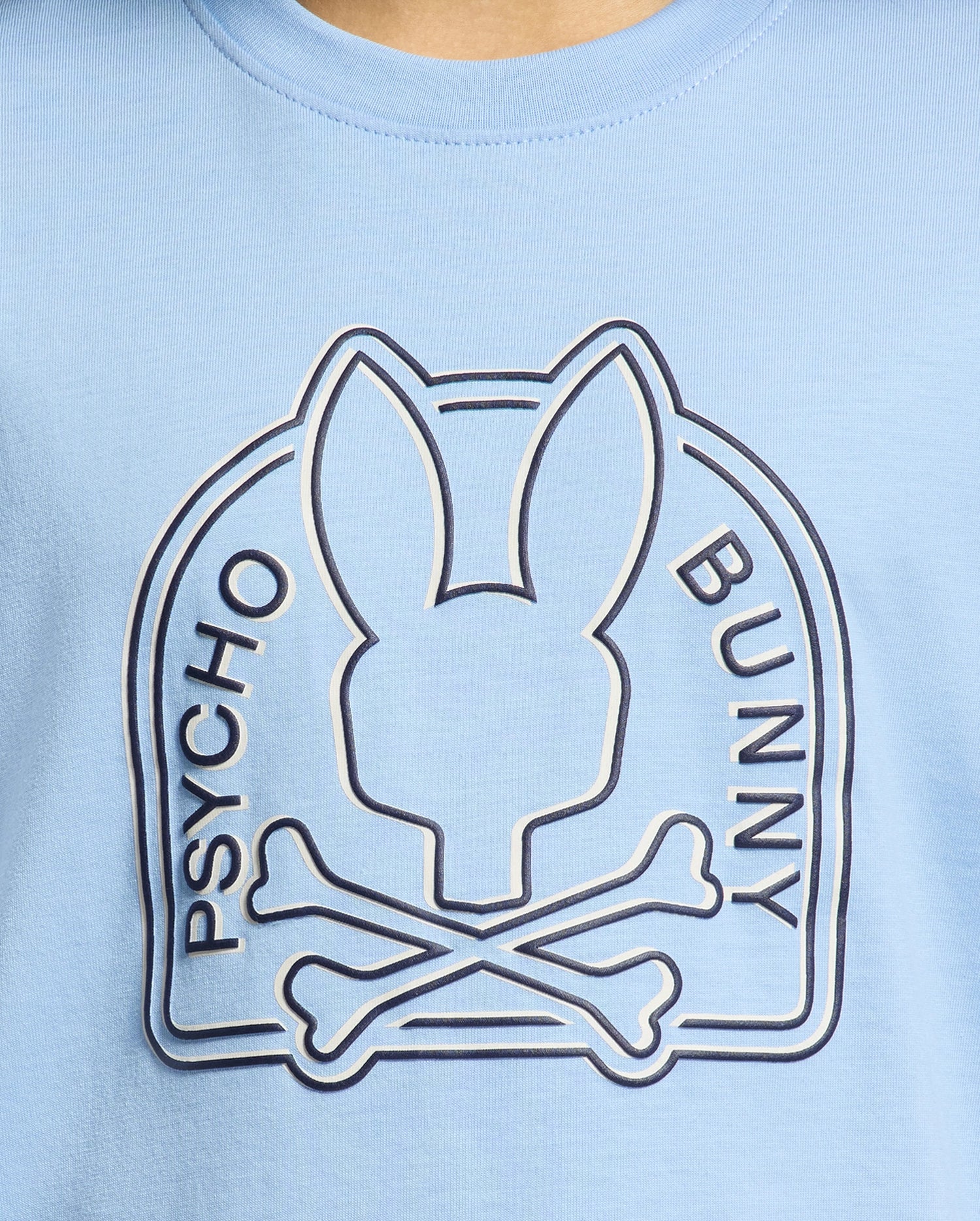 The Psycho Bunny KIDS MELBOURNE GRAPHIC TEE (B0U410F200) in light blue showcases a stylized bunny head above crossed bones with the text "Psycho Bunny." Made from 100% Pima cotton, it is soft and eco-friendly.