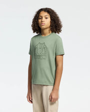 A person with curly hair stands against a plain background, wearing a green KIDS MELBOURNE GRAPHIC TEE (B0U410F200) by Psycho Bunny and beige pants.