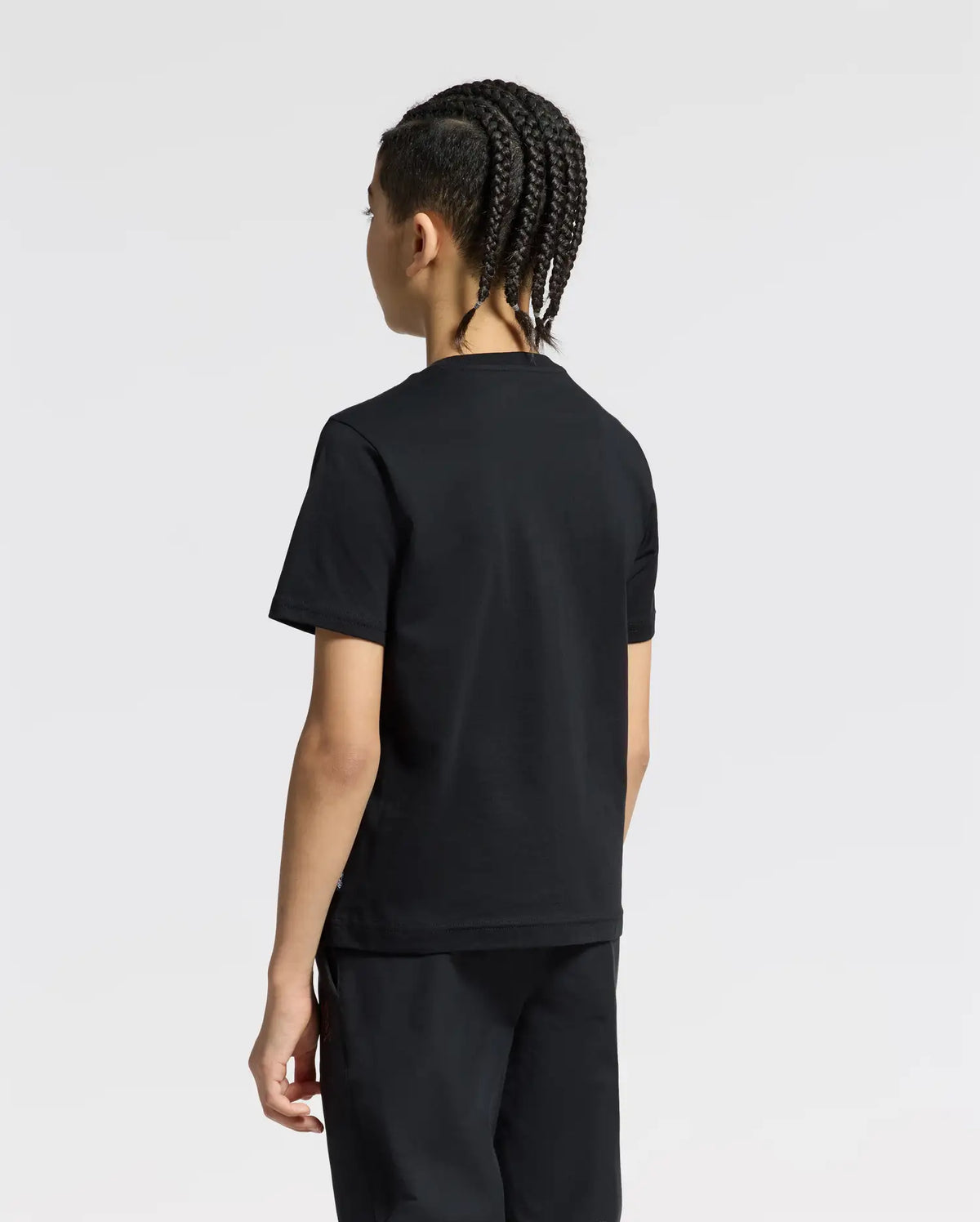 A person with braided hair, clad in a black KIDS SILVERDALE GRAPHIC TEE by Psycho Bunny and matching pants, stands facing away against a plain white background.