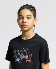 A young person with braided hair wears the KIDS SILVERDALE GRAPHIC TEE by Psycho Bunny, a black Pima cotton shirt showcasing colorful bunny graphics across the chest. The water-based print stands out against the light gray background.