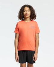 A child with curly hair faces forward wearing a regular fit, bright orange Psycho Bunny KIDS SYDNEY BACK GRAPHIC TEE (B0U509F200) and black shorts against a plain white background.