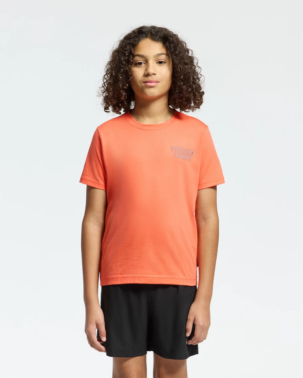 A child with curly hair faces forward wearing a regular fit, bright orange Psycho Bunny KIDS SYDNEY BACK GRAPHIC TEE (B0U509F200) and black shorts against a plain white background.