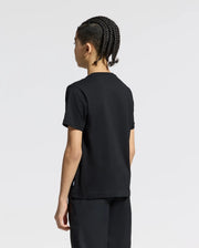 A person with braided hair is standing against a plain light background, wearing a black Psycho Bunny KIDS ANDROS GRAPHIC TEE (B0U525F200) made in Peru from soft Pima cotton.