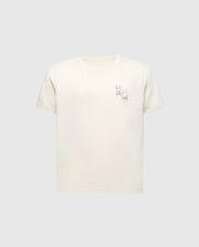 The Psycho Bunny KIDS ELLIOT FRONT BACK GRAPHIC TEE (B0U605F200) is a light beige Pima cotton shirt featuring an eco-friendly water-based print of a simple cartoon rabbit line drawing on the upper left, set against a plain grey background.