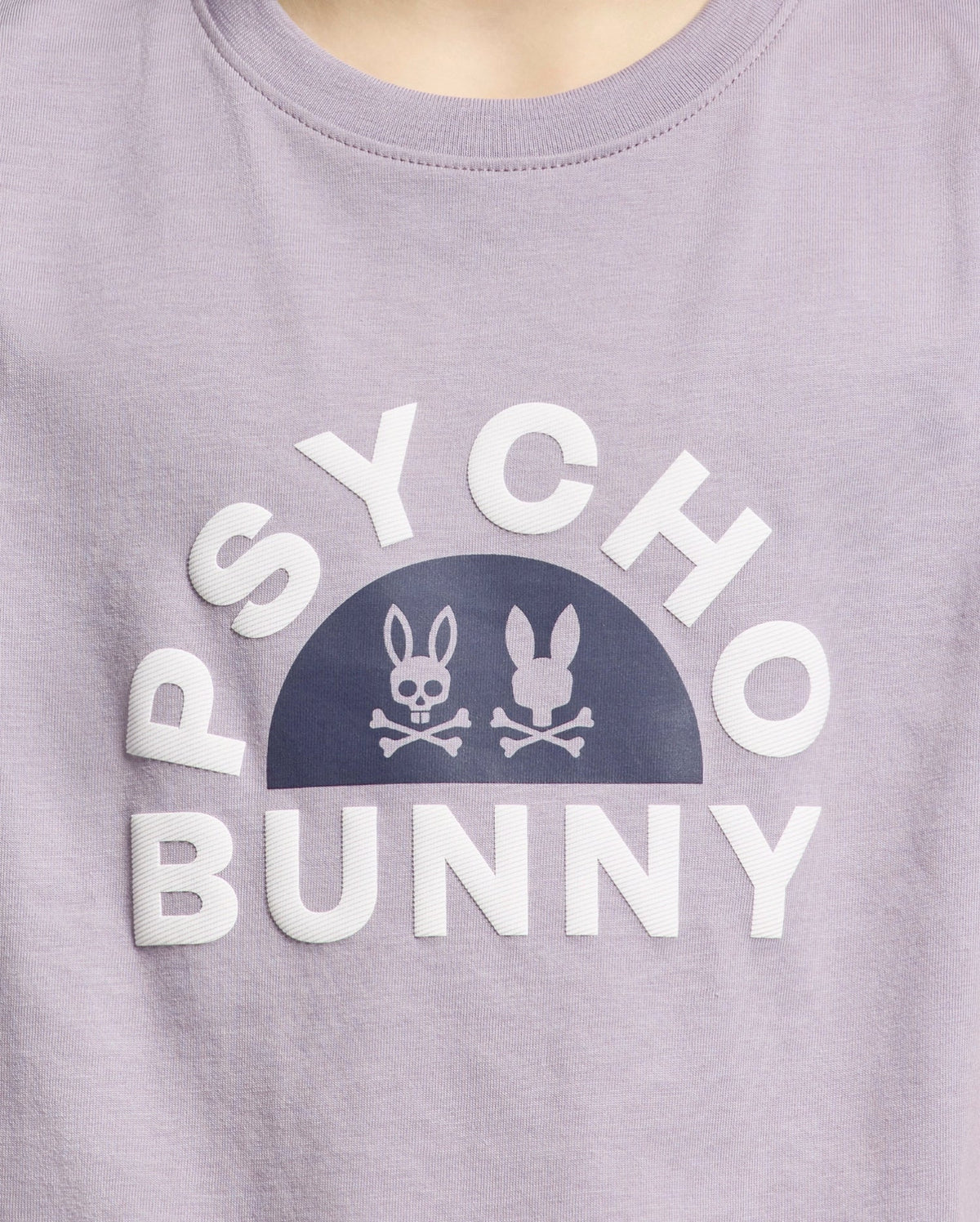 The KIDS GOLDIE GRAPHIC TEE - B0U606F200 from Psycho Bunny, made of luxurious Peruvian Pima cotton, features "Psycho Bunny" in white around a half-circle with two stylized bunnies and crossed bones forming a striking graphic on a lavender backdrop.