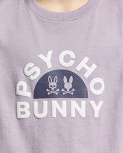 The KIDS GOLDIE GRAPHIC TEE - B0U606F200 from Psycho Bunny, made of luxurious Peruvian Pima cotton, features "Psycho Bunny" in white around a half-circle with two stylized bunnies and crossed bones forming a striking graphic on a lavender backdrop.