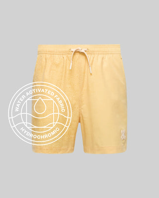 The Psycho Bunny MENS SAMOS HYDROCHROMIC PRINTED SWIM TRUNK (B6W453F200) features a light yellow shade, subtle bunny pattern, drawstring waist, white bunny logo on the left leg, and a "Water Activated Fabric Hydrochromic Technology" label.