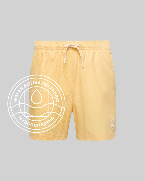 The Psycho Bunny MENS SAMOS HYDROCHROMIC PRINTED SWIM TRUNK (B6W453F200) features a light yellow shade, subtle bunny pattern, drawstring waist, white bunny logo on the left leg, and a "Water Activated Fabric Hydrochromic Technology" label.