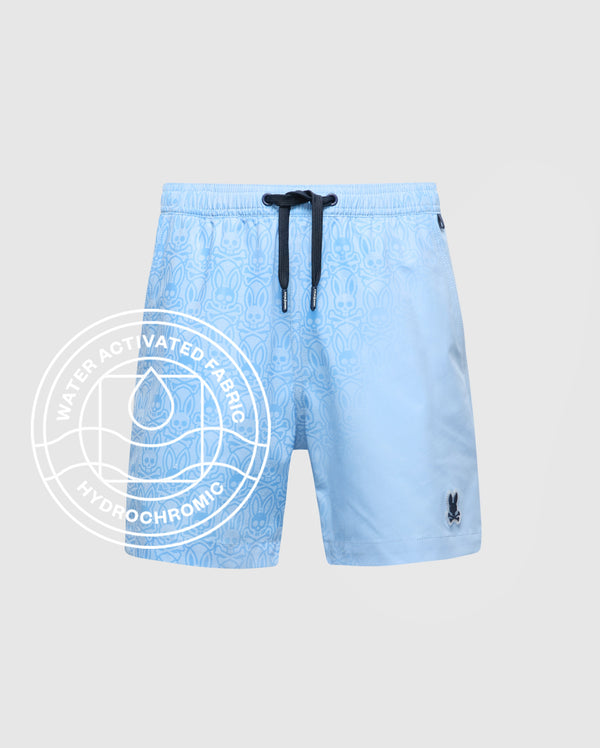 The KIDS SAMOS HYDROCHROMIC PRINTED SWIM TRUNK by Psycho Bunny features a light blue pattern, black drawstring, and bunny logo. Water-activated Hydrochromic fabric reveals hidden designs—ideal with your waterproof bag for pool days.
