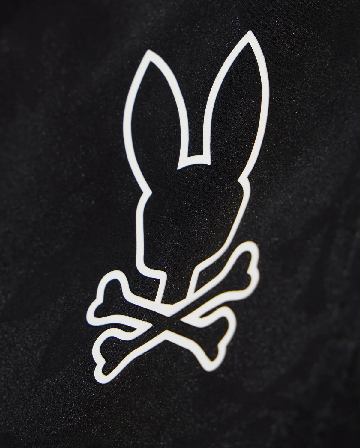 A black background with a white graphic design featuring the silhouette of a bunny's head, complete with large upright ears, positioned above two crossed bones. Perfect for customizing your waterproof bag or Psycho Bunny KIDS PARKER HYDROCHROMIC SWIM TRUNK - B0W646C200.