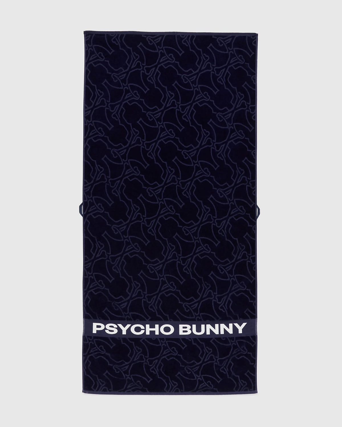 The Psycho Bunny TOWEL - B6A287F200 is a navy rectangular terrycloth cotton towel featuring an abstract bunny pattern and "PSYCHO BUNNY" in bold white letters along the bottom edge.